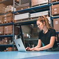 a woman is working on a laptop in a warehouse